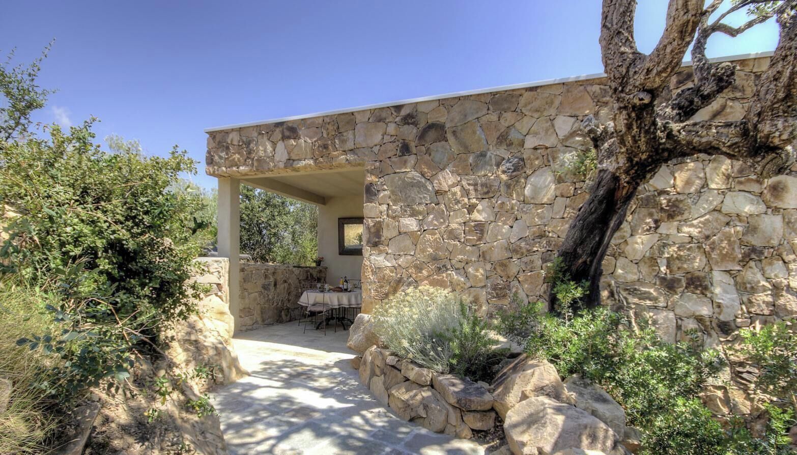 A stone building with a covered outdoor seating area and a natural landscape.