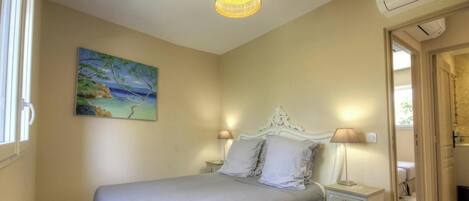 Un dormitorio con cama, lámparas de noche, un cuadro en la pared y una puerta que da a otra habitación.