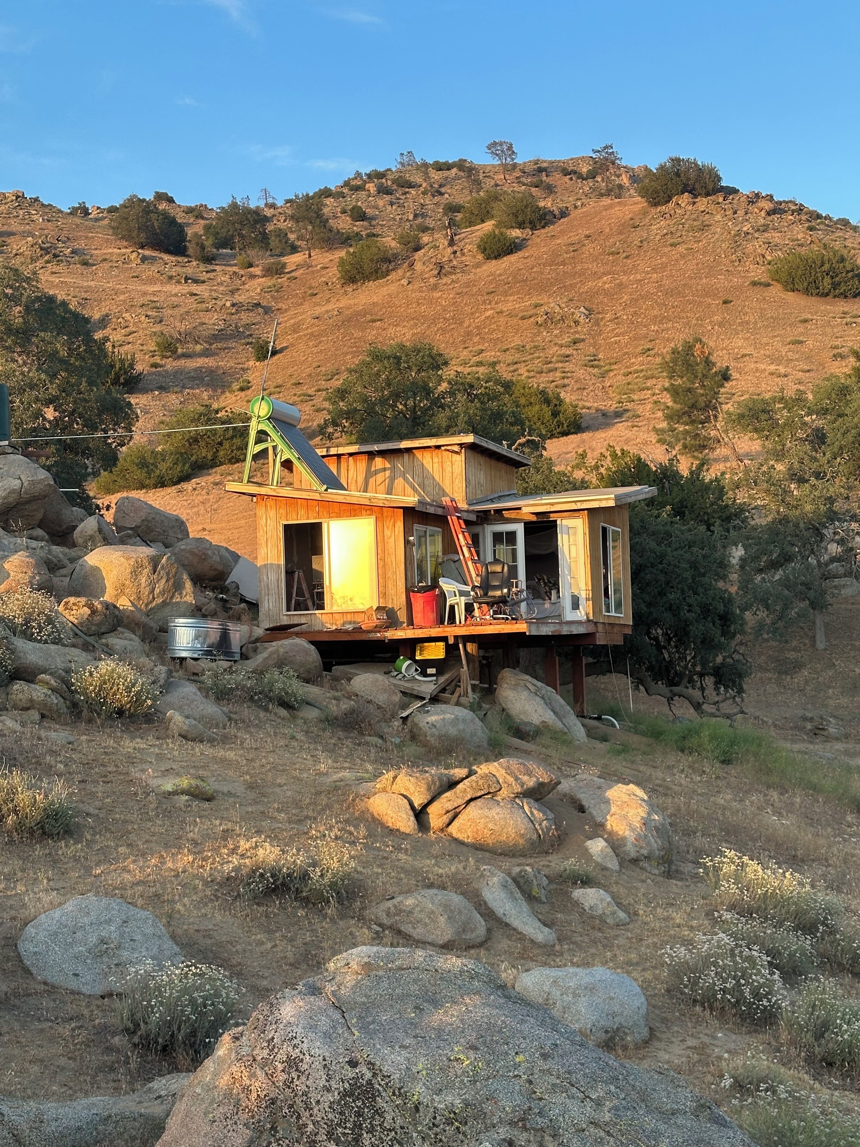 A rustic cabin with a wooden exterior, a metal roof, and a ladder leading to the entrance.