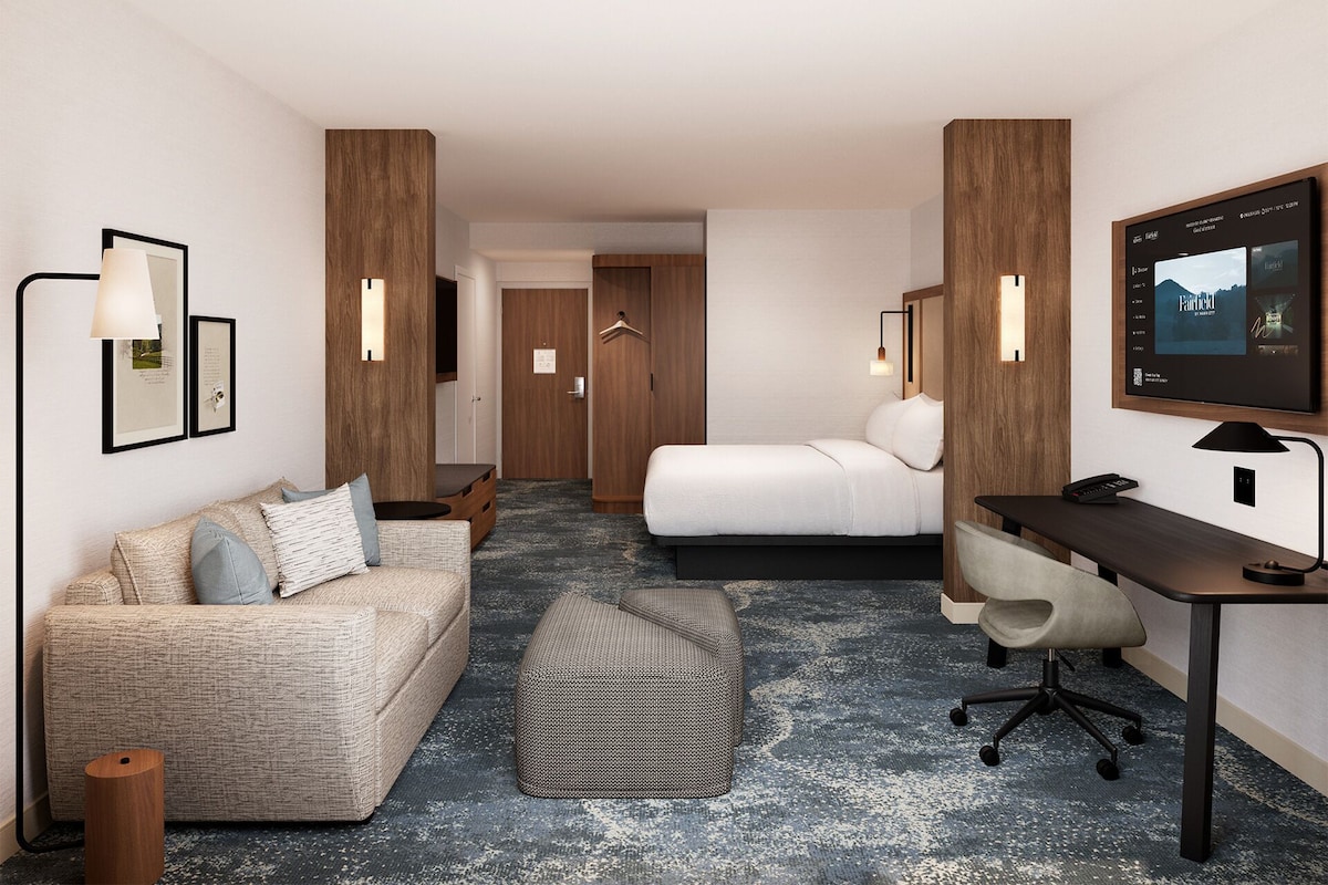 Une chambre d’hôtel équipée d’un canapé, d’un lit, d’un bureau, d’une chaise, d’une télévision et d’une petite table.