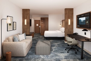 Habitación de hotel con sofá, cama, escritorio, silla, televisor y una mesita.