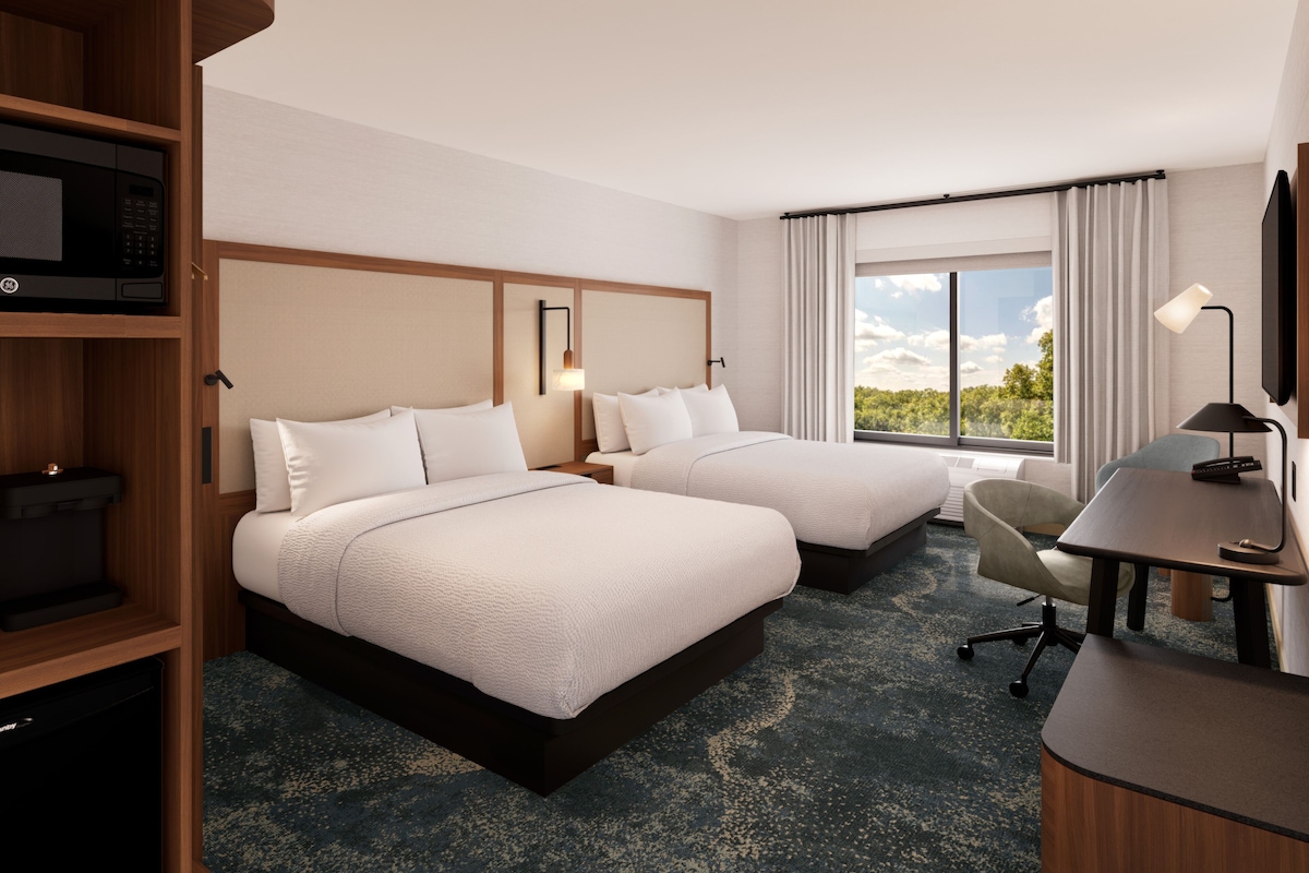 Une chambre d’hôtel avec deux lits, un bureau, une chaise, une télévision et une fenêtre donnant sur un paysage agréable.