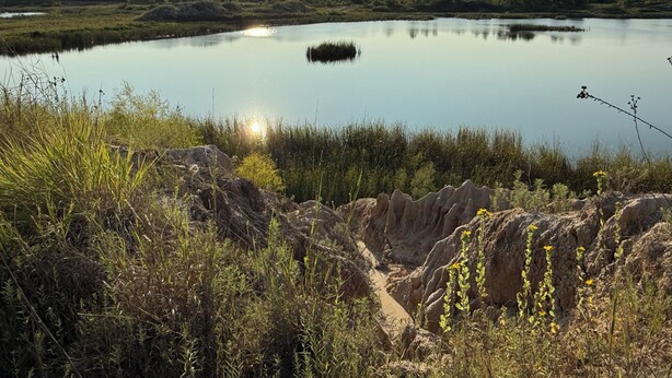 A natural landscape with a calm lake, rocky terrain, and sparse vegetation.