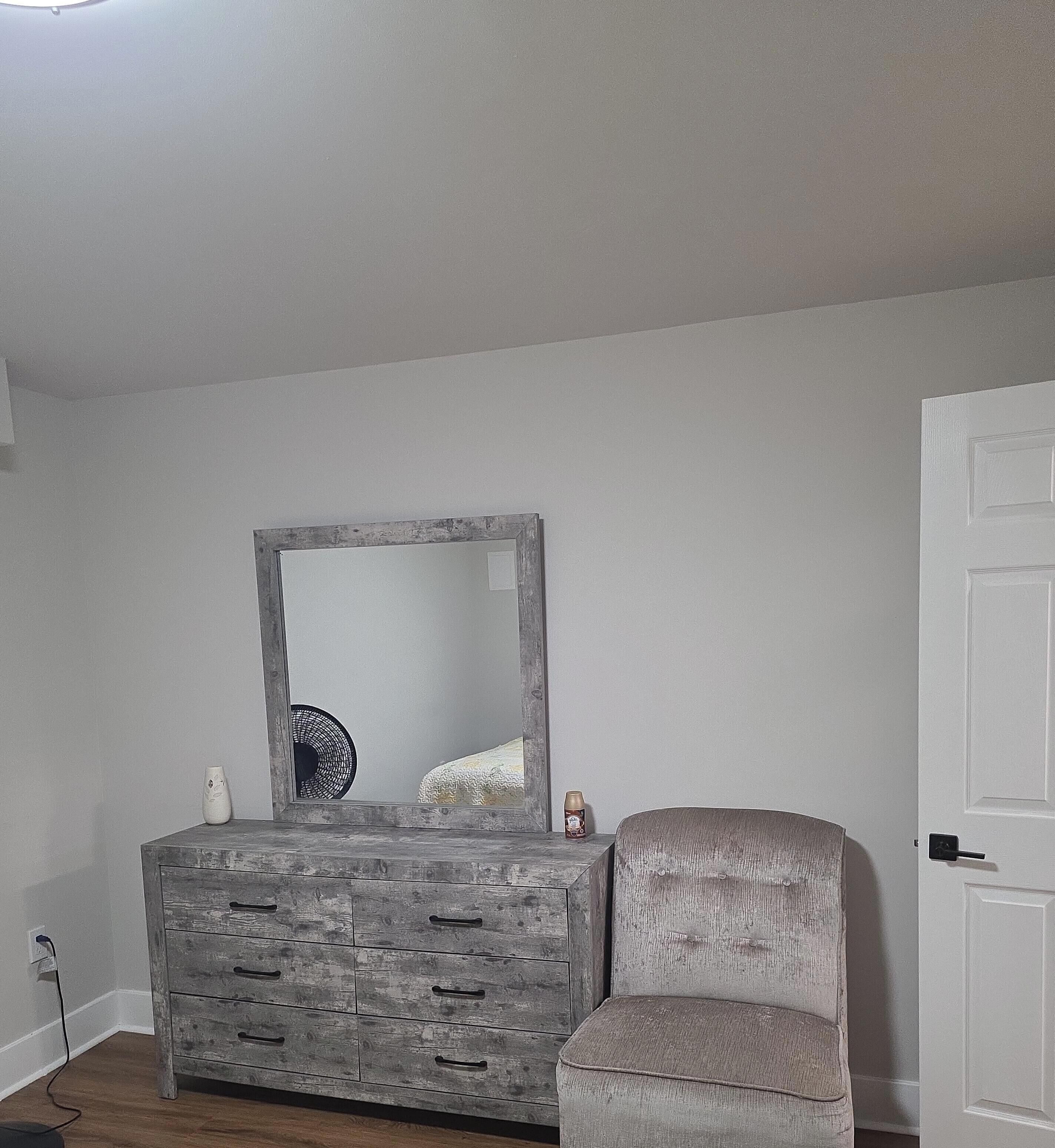 A room with a wooden dresser, a chair, a mirror, and a white door.