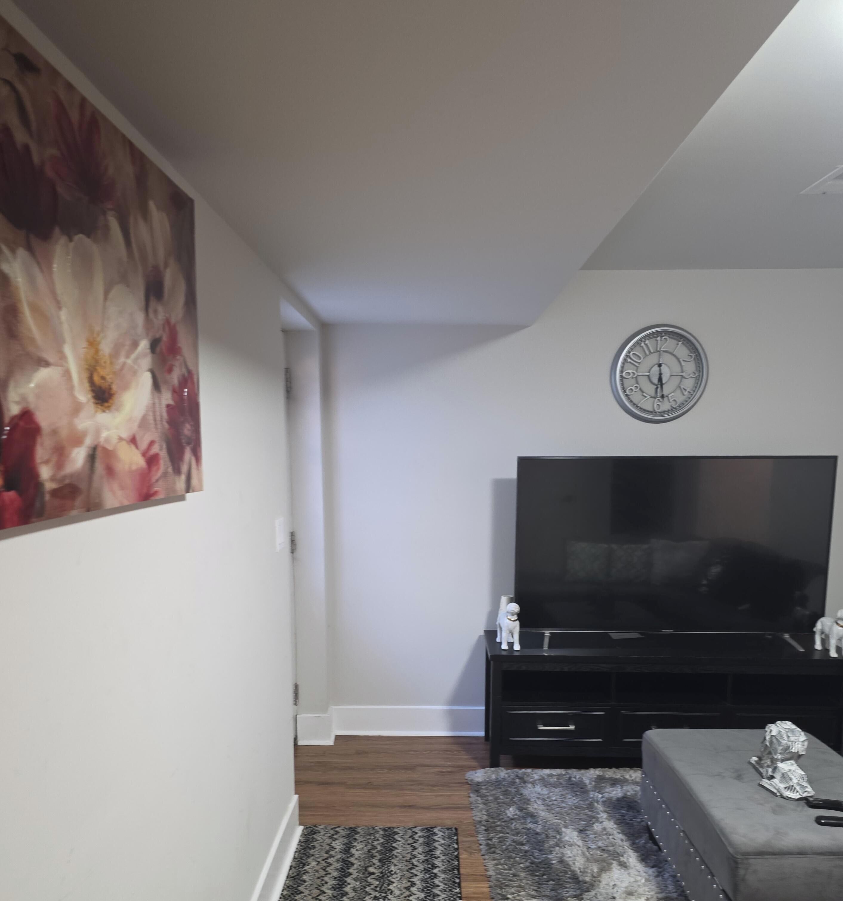 A living room with a large flat-screen TV, a clock on the wall, and a painting.