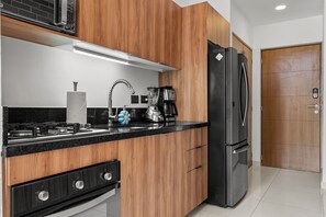 Eine moderne Küche mit Holzschränken, einem schwarzen Kühlschrank, einer Kaffeemaschine und einem Gasherd.