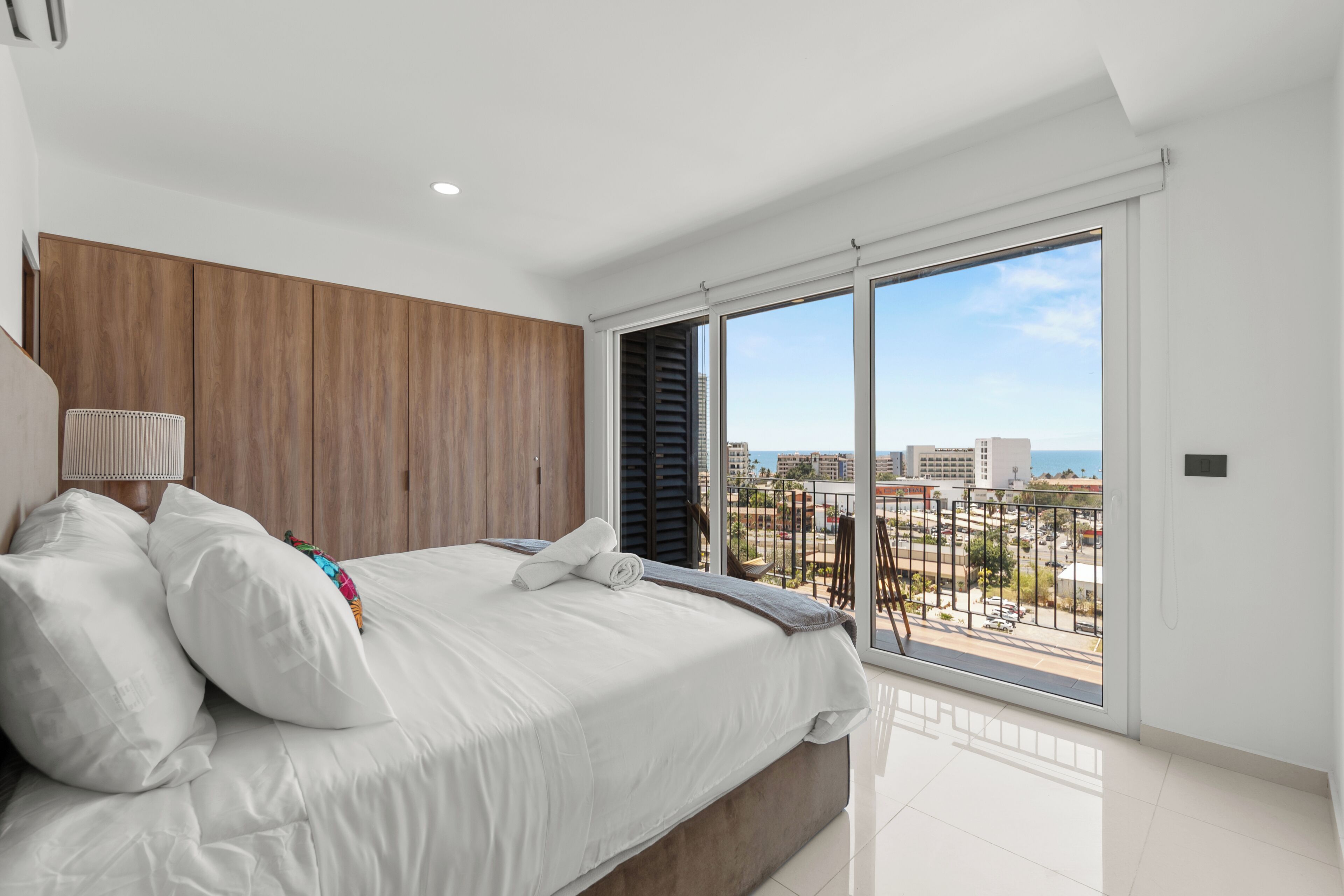 Ein modernes Schlafzimmer mit einem großen Bett, Holzvertäfelung, Blick auf die Stadt und einem Balkon.