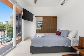 Ein modernes Schlafzimmer mit Bett, Fernseher, Holzschrank und einem Balkon mit Stuhl.