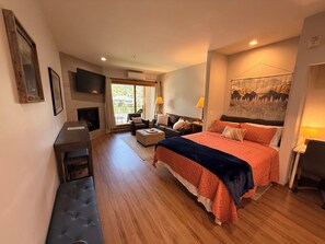 A spacious bedroom with a large bed, a seating area with a sofa and armchairs, a television, and a view through the window. - The Perfect Ski Escape - Steps to the Gondola (Steamboat Springs)