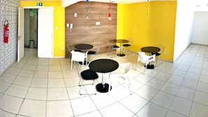 Un espace repas moderne avec des murs jaunes, plusieurs tables rondes et des chaises blanches.
