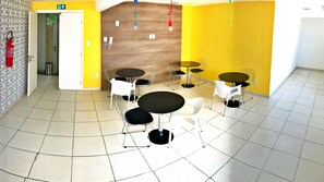 Uma sala de jantar moderna com paredes amarelas, várias mesas redondas e cadeiras brancas.