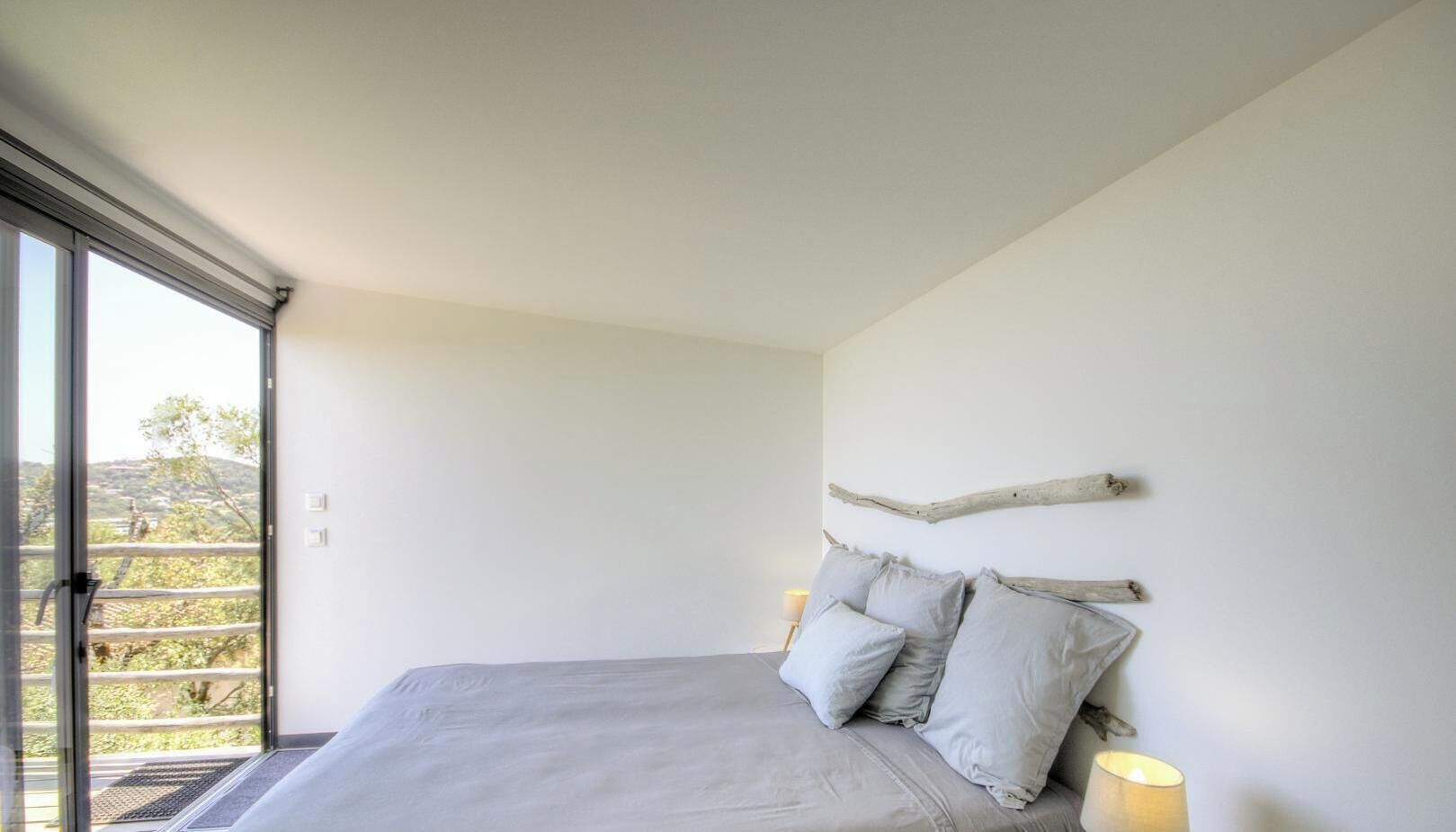 A bedroom with a bed, pillows, a nightstand, and a window with a view.