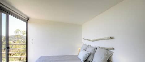 A bedroom with a bed, pillows, a nightstand, and a window with a view.