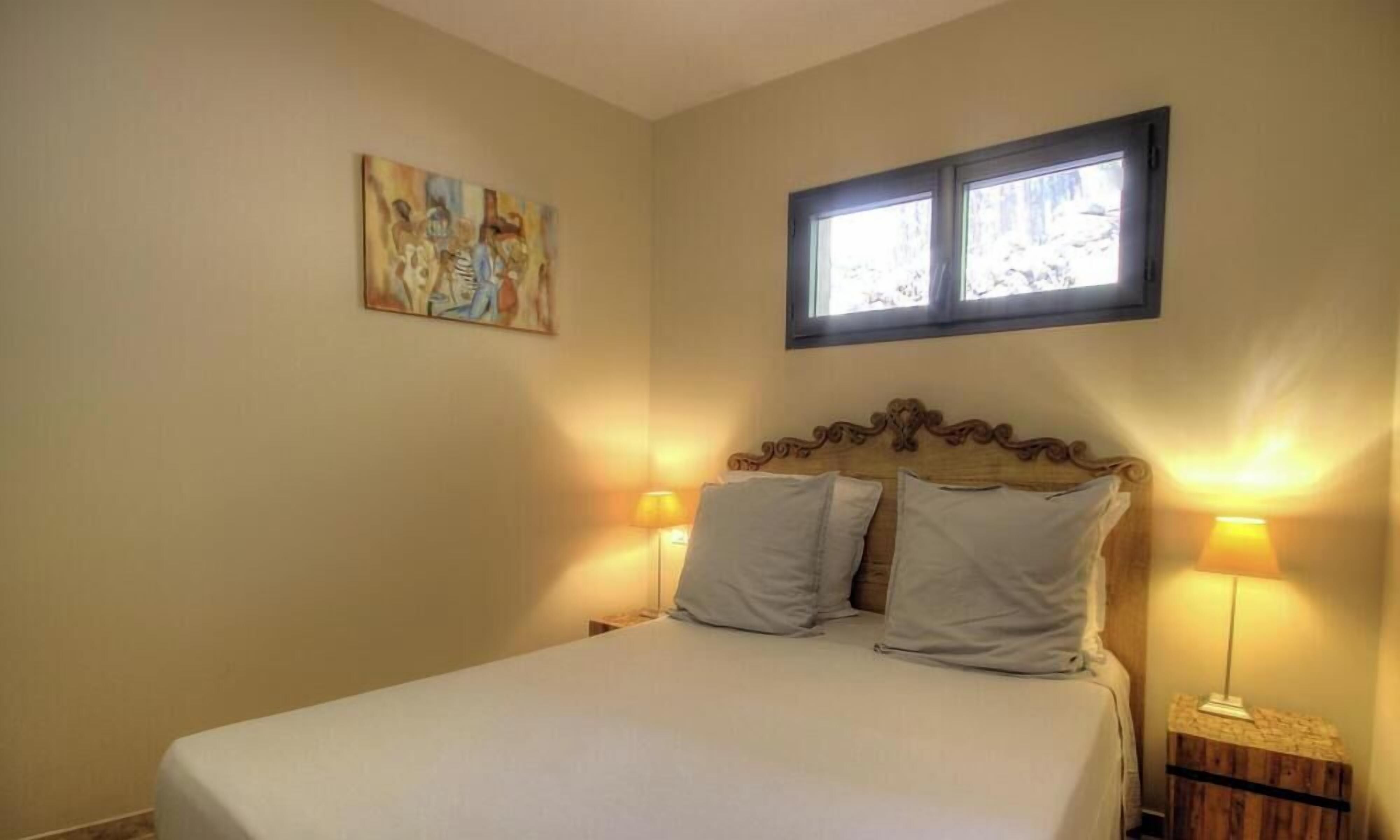 Ein Schlafzimmer mit einem Bett, zwei Nachttischlampen, einem Fenster und einem Bild an der Wand.