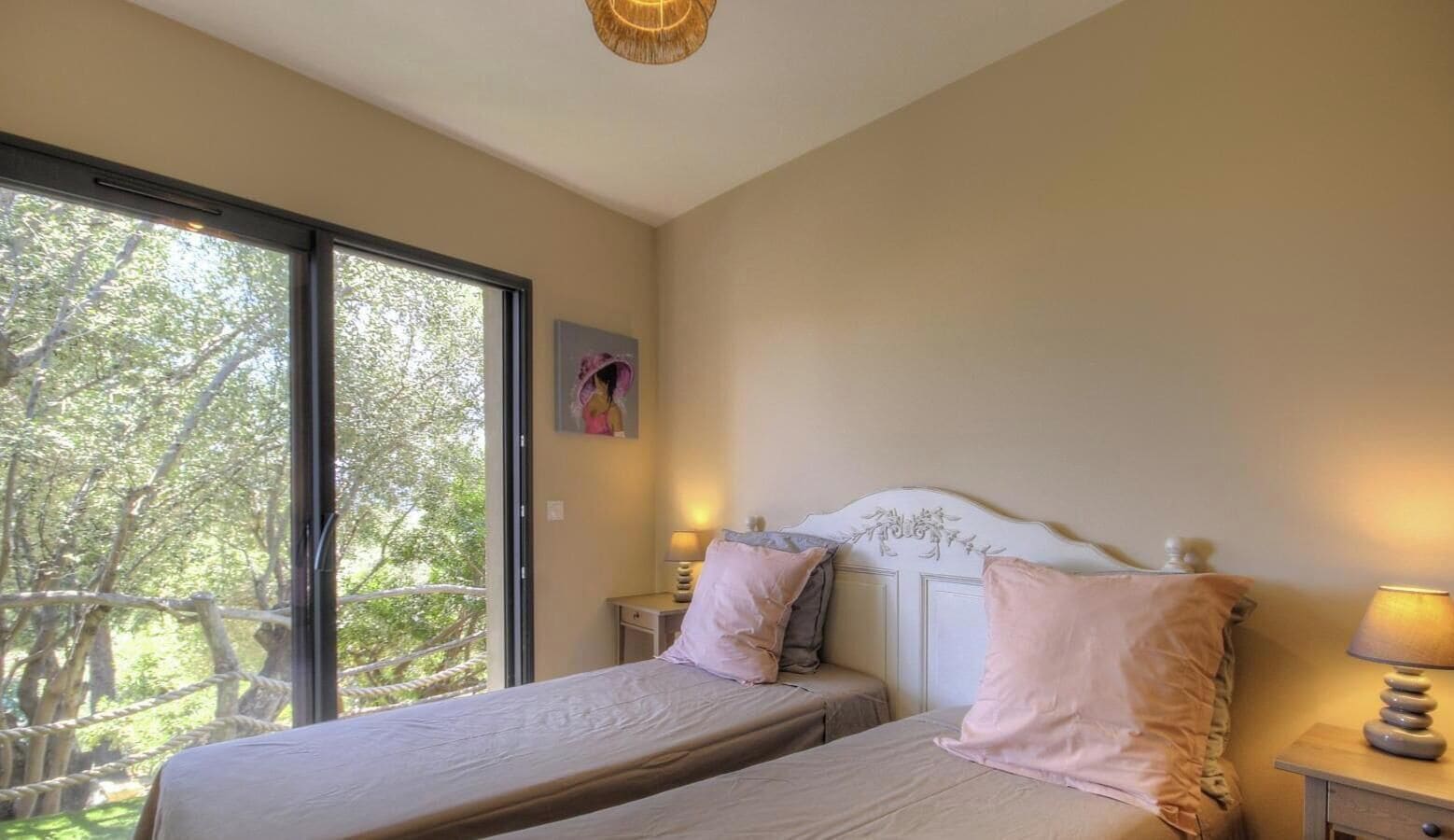 Ein Schlafzimmer mit einem Bett, zwei Nachttischen und einem Fenster mit Blick auf Bäume.