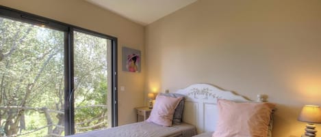 Ein Schlafzimmer mit einem Bett, zwei Nachttischen und einem Fenster mit Blick auf Bäume.