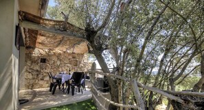 An outdoor dining area with stone walls, a table with chairs, and a view of trees. - Alba - Porto Vecchio (PORTO VECCHIO)