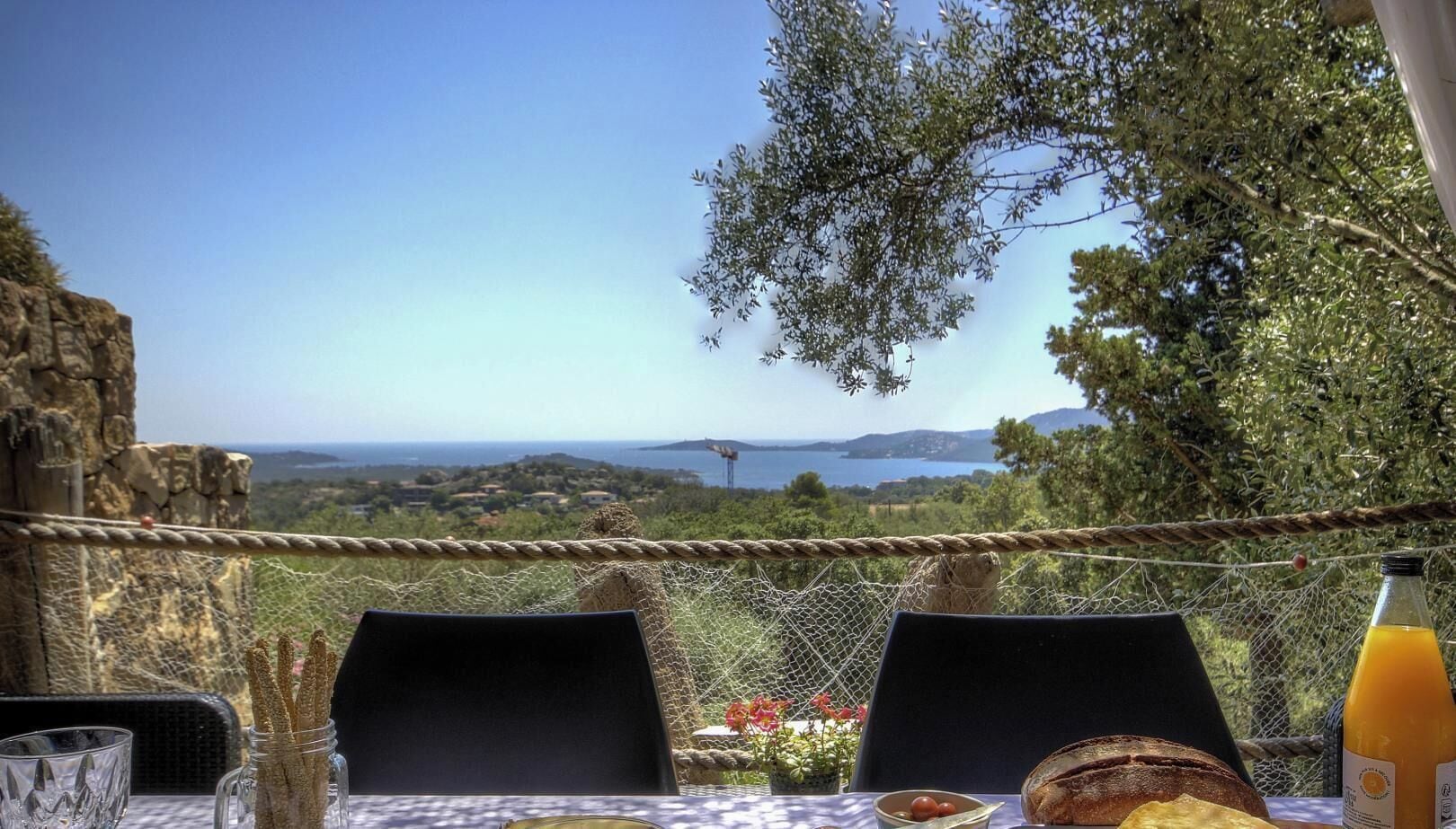 A table set outdoors with a view of a coastal landscape, including a rope barrier and a bottle of orange juice.