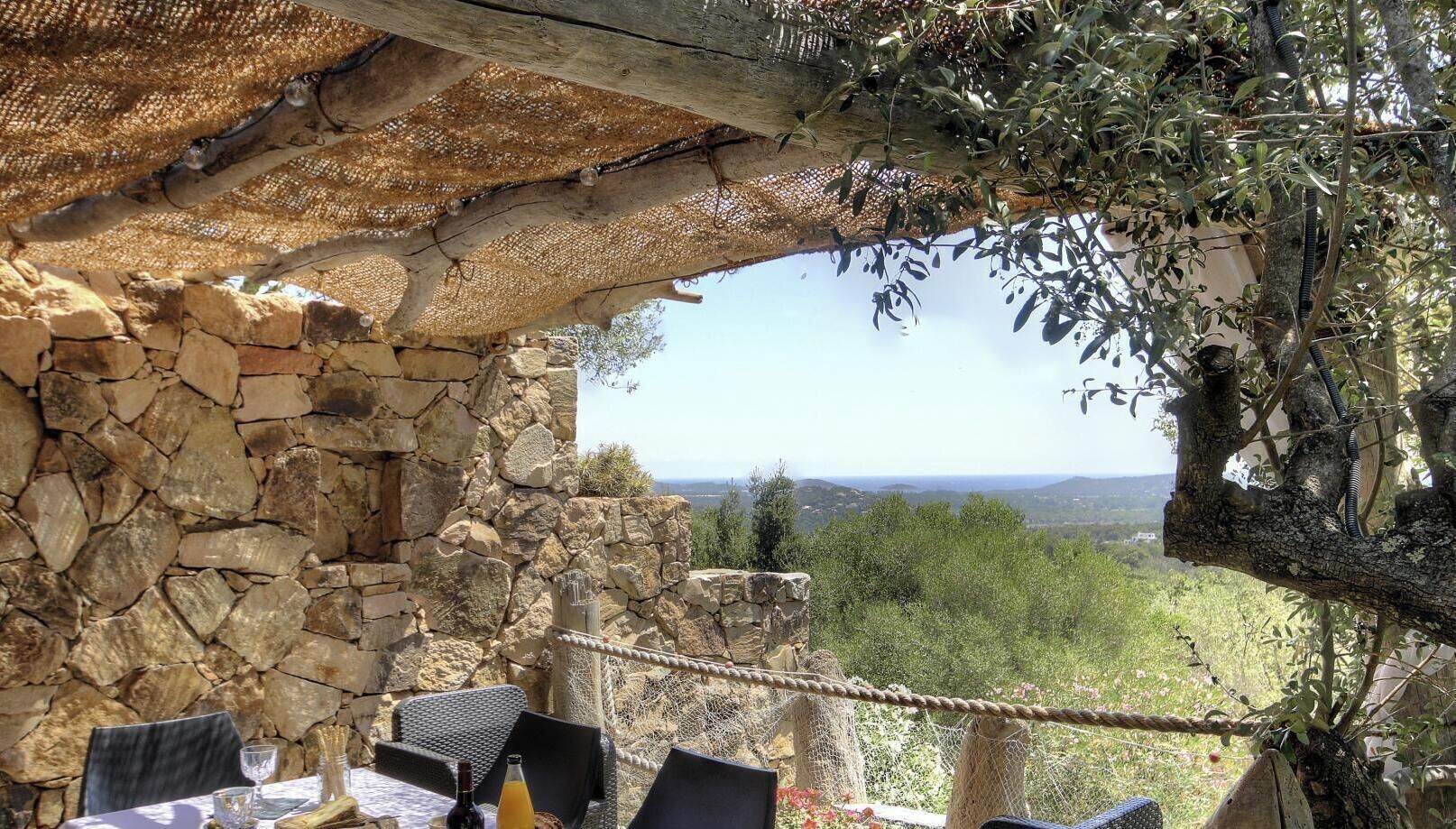 A stone wall with a table and chairs, a rope barrier, and a view of a landscape with trees and hills.