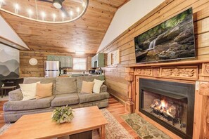 A cozy living room with a fireplace, a sofa, and a television mounted above it. - Cozy Sevierville Cabin - Hot Tub & Fireplace (Sevierville)