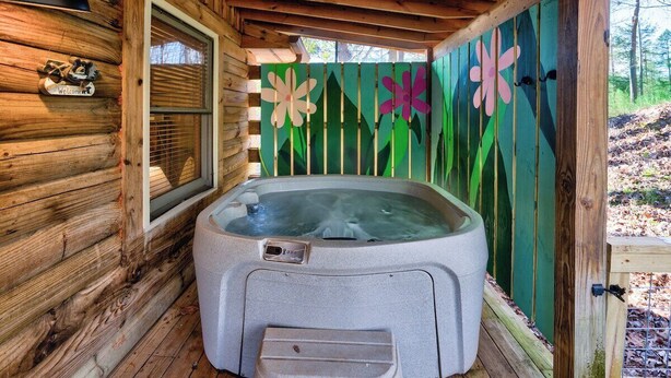 Eine Holzjagdhaushälfte mit Whirlpool, einem Fenster und einem grünen Zaun mit Blumendekorationen.