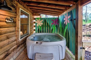 Une cabane en bois avec un jacuzzi, une fenêtre et une clôture verte agrémentée de décorations florales.