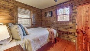 Ein Schlafzimmer einer Holzhütte mit einem Bett, Kissen, einer Decke und einem Deckenventilator.