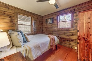 Ein Schlafzimmer einer Holzhütte mit einem Bett, Kissen, einer Decke und einem Deckenventilator.