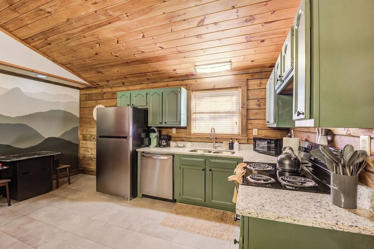 A kitchen with wooden ceiling, green cabinets, stainless steel appliances, and a granite countertop.