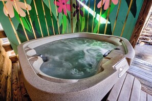 Uma banheira de hidromassagem com painel de controle, rodeada por um deck de madeira e uma parede com desenhos florais.