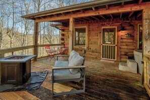 A wooden cabin with a covered porch, a fire pit, a sofa, and a table. - Cozy Sevierville Cabin - Hot Tub & Fireplace (Sevierville)