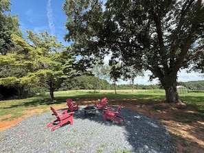 An outdoor seating area with red chairs and a fire pit surrounded by gravel, under a large tree.