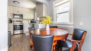 Een moderne keuken met roestvrijstalen apparatuur, een eettafel met stoelen en een raam met zonwering.