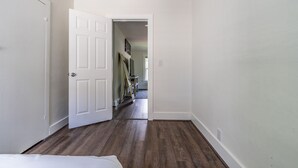 Een gang met een houten vloer, witte muren en een gedeeltelijk open deur naar een andere kamer.