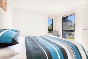 Ein Schlafzimmer mit einem Bett, zwei Fenstern und Blick ins Freie.