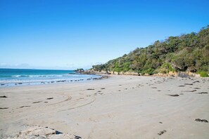 A beach with a clear sky, sandy shore, and a forested hill in the background.