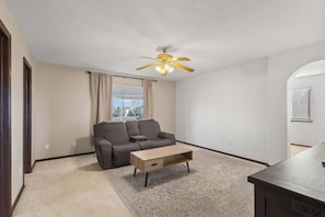 A living room with a sofa, a coffee table, a ceiling fan, and a window with curtains. - Your Colorado Springs Home Base! (Colorado Springs)