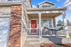A two-story house with a brick facade, a red door, and a white porch with a railing. - Your Colorado Springs Home Base! (Colorado Springs)