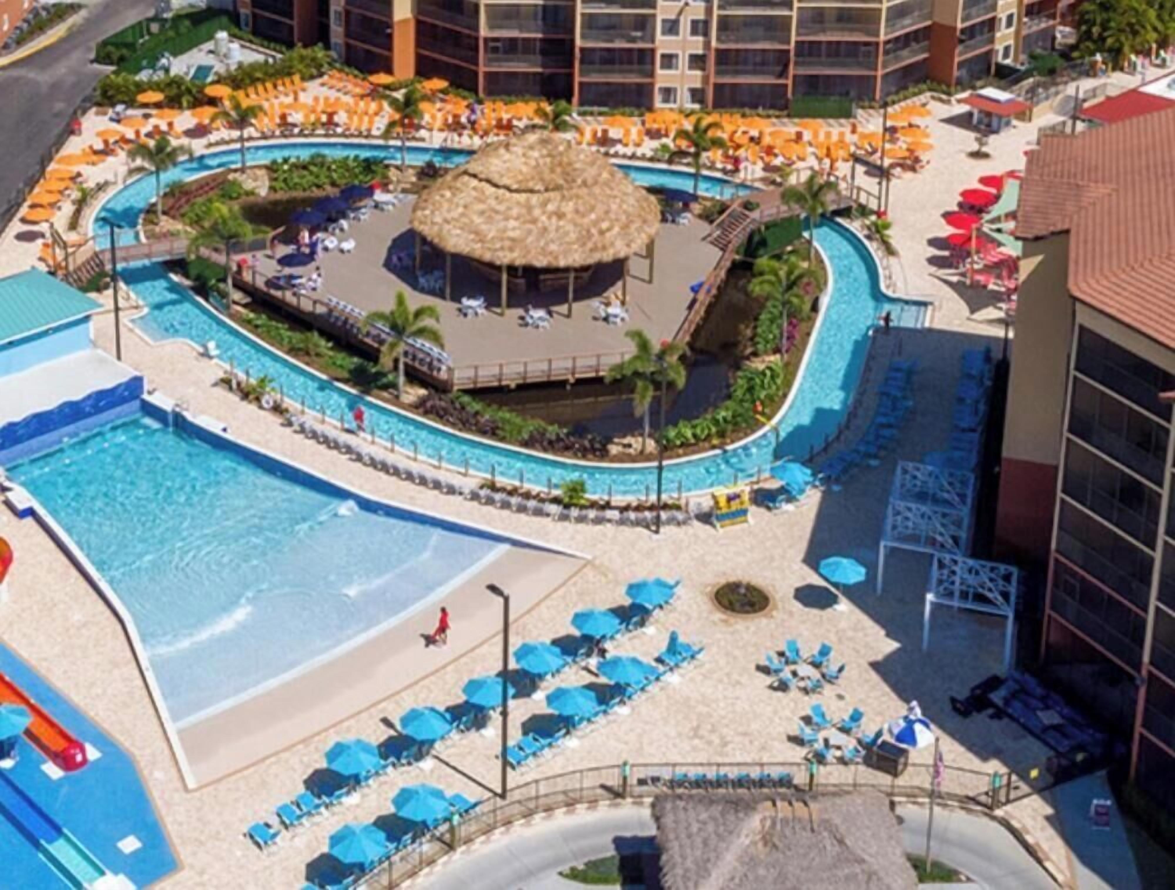 Ein Resort mit großem Pool, Liegestühlen und einem strohgedeckten Gebäude.