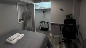 A compact hotel room with a bed, a desk, a chair, and a small window. - 2BR Avondale Apt: Free Parking + Steps to Blueline (Chicago)