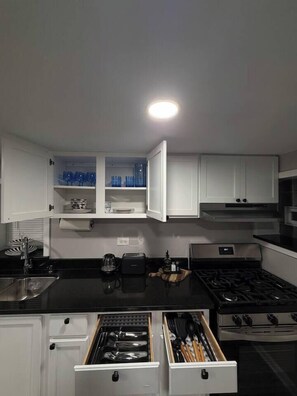 A kitchen with white cabinets, a black countertop, a stove, and a drawer with utensils. - 2BR Avondale Apt: Free Parking + Steps to Blueline (Chicago)