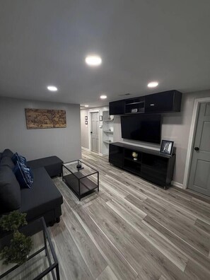 A modern living room with a sectional sofa, a glass coffee table, and a flat-screen TV on a black entertainment unit. - 2BR Avondale Apt: Free Parking + Steps to Blueline (Chicago)