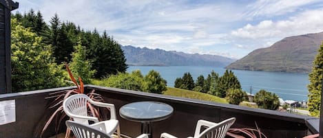 A balcony with a table and chairs, overlooking a lake and mountains.