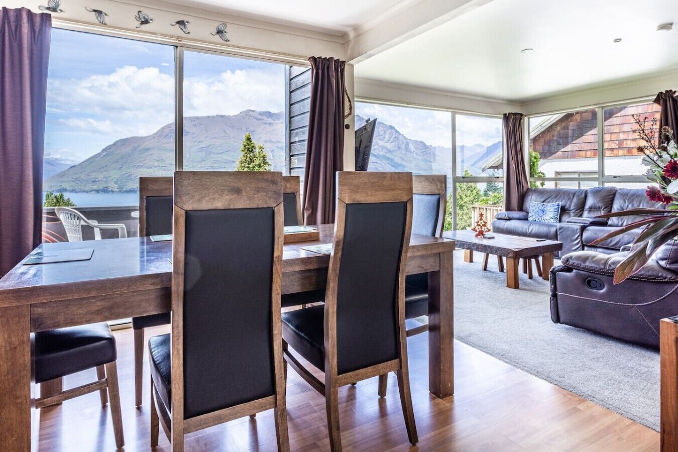 Un salon moderne avec un coin repas, de grandes fenêtres offrant une vue sur les montagnes et un espace salon confortable.