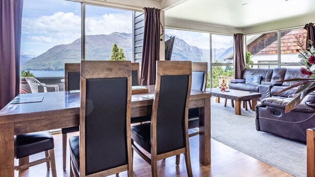 Ein modernes Wohnzimmer mit Essbereich, großen Fenstern und Blick auf die Berge sowie einer gemütlichen Sitzecke.