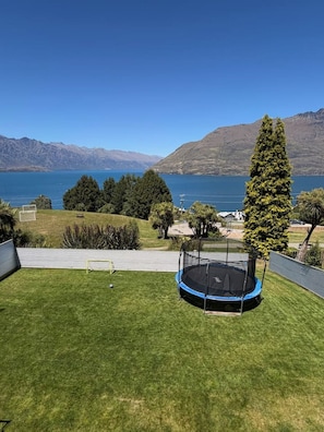 Une zone herbeuse avec un trampoline, une vue dégagée sur un lac et des montagnes en arrière-plan.