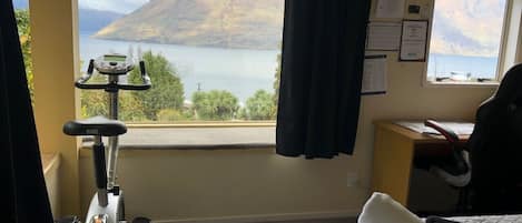 A hotel room with a bed, a desk, a chair, a treadmill, and a window with a mountain view.