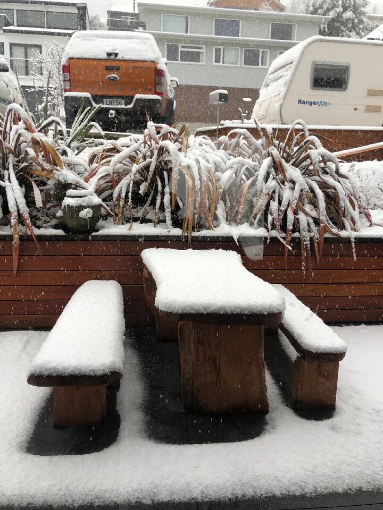 A snowy outdoor seating area with benches and a wooden wall.