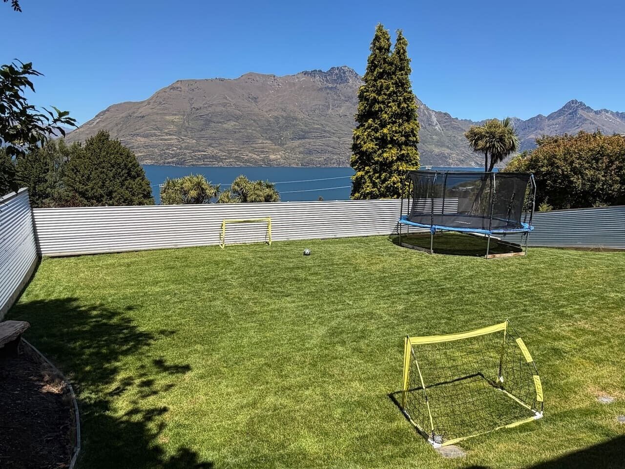 A backyard with a goalpost, a trampoline, and a view of mountains and a lake.