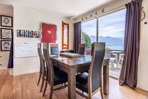 A dining area with a wooden table, chairs, and a whiteboard with a message. - Lakeview Family Home | Spa Pool | Sleeps 14 | 5 Min Town (Queenstown)